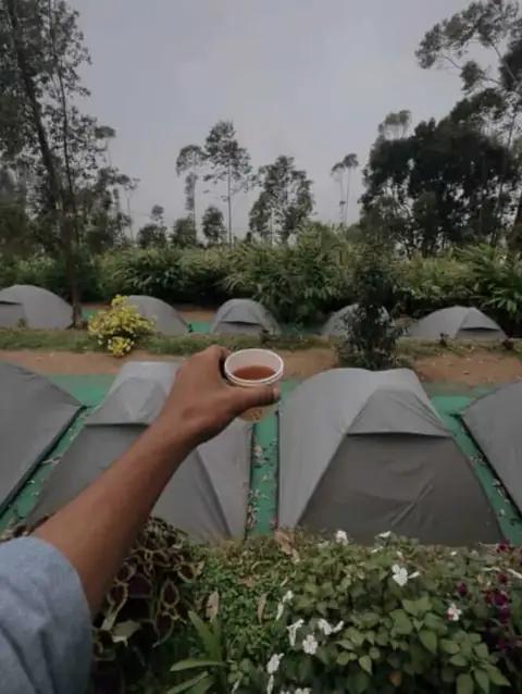 Hand holding a cup of tea beside camp tents
